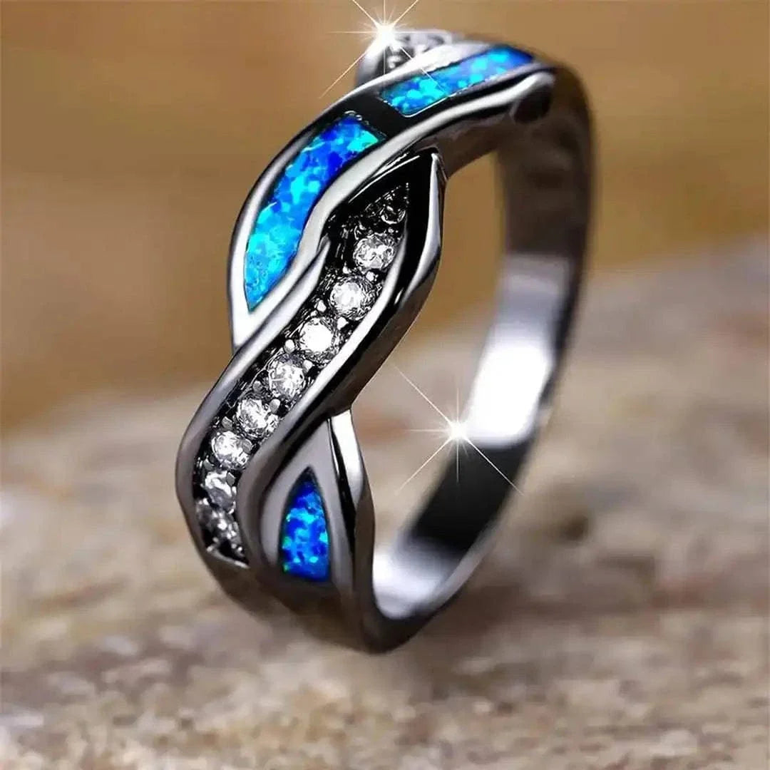 Bague Thessia Lunebray noire, deux inserts bleu opale et ailettes serties de pierres claires.