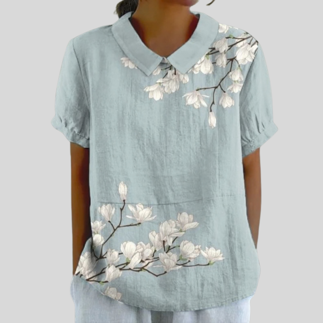 Blouse bleu clair, col et manches courtes, fleurs placées brodées sur la poitrine