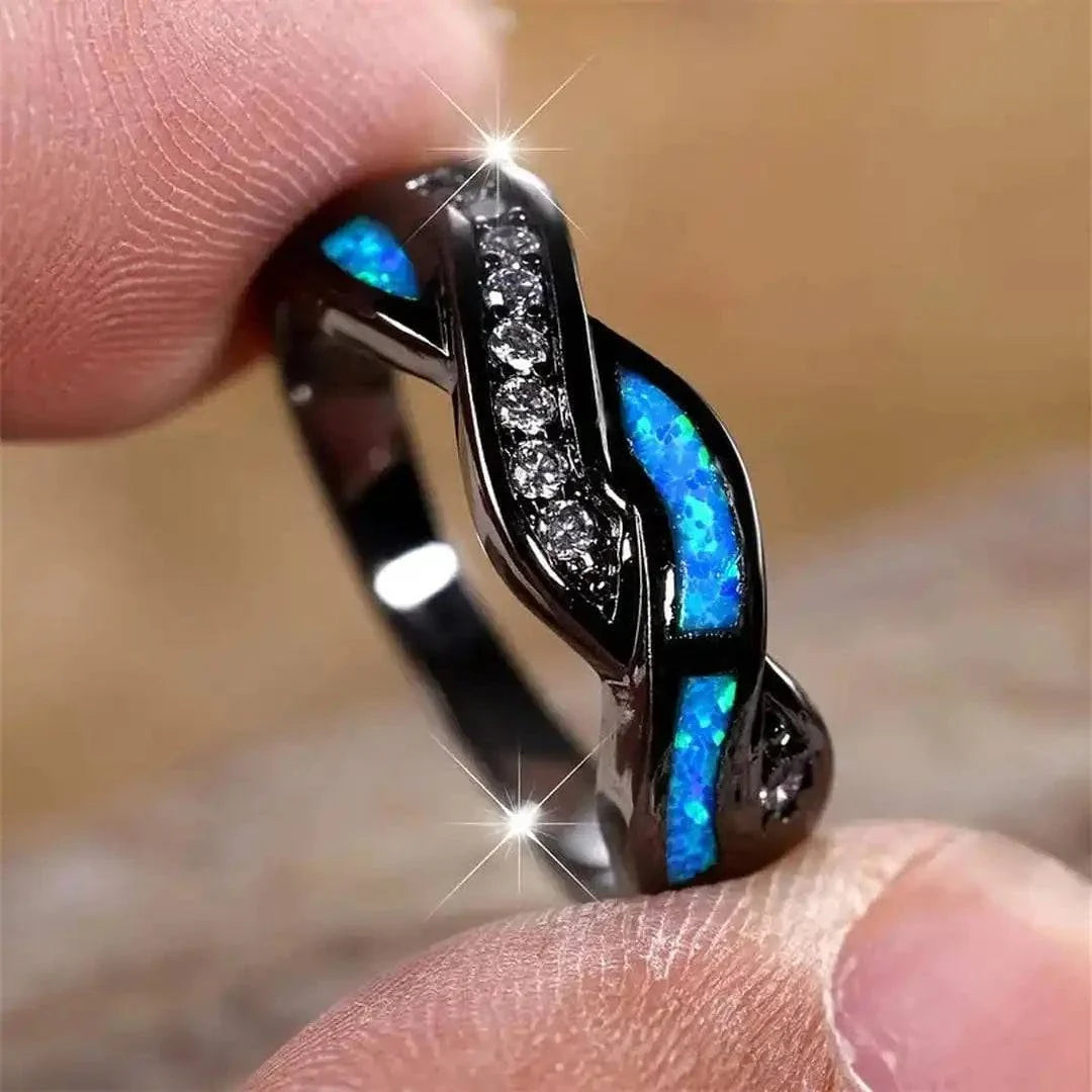 Bague Thessia Lunebray noire, gros insert bleu et pavé de petites pierres claires.