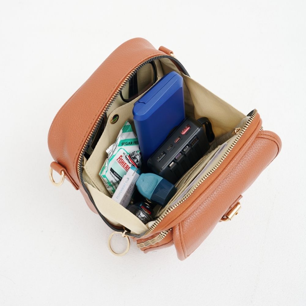 Sac bandoulière en cuir brun, zip ouvert, compartiments pour accessoires.