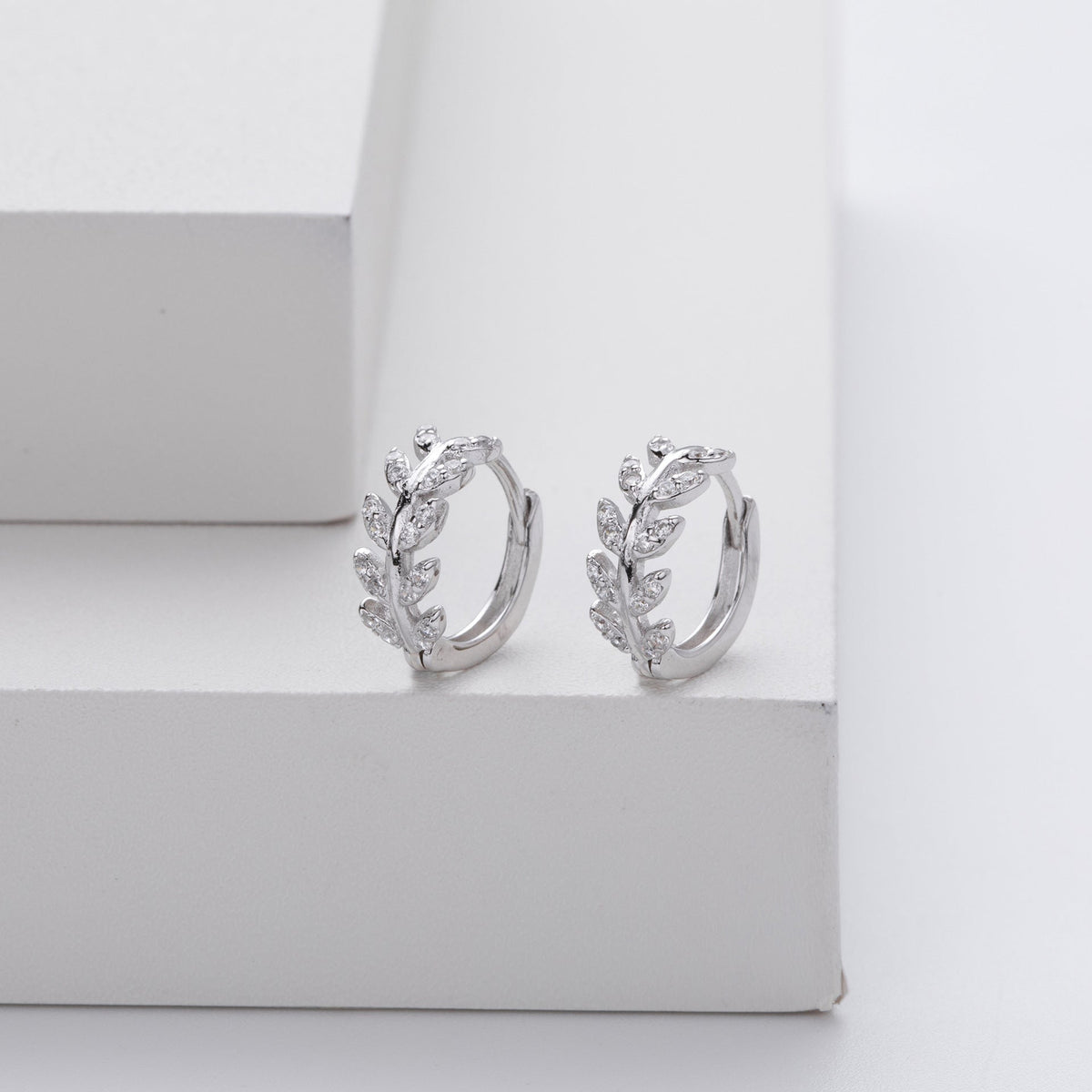 Boucles d’oreilles créoles argent en forme de feuilles, décorées de petites pastilles.