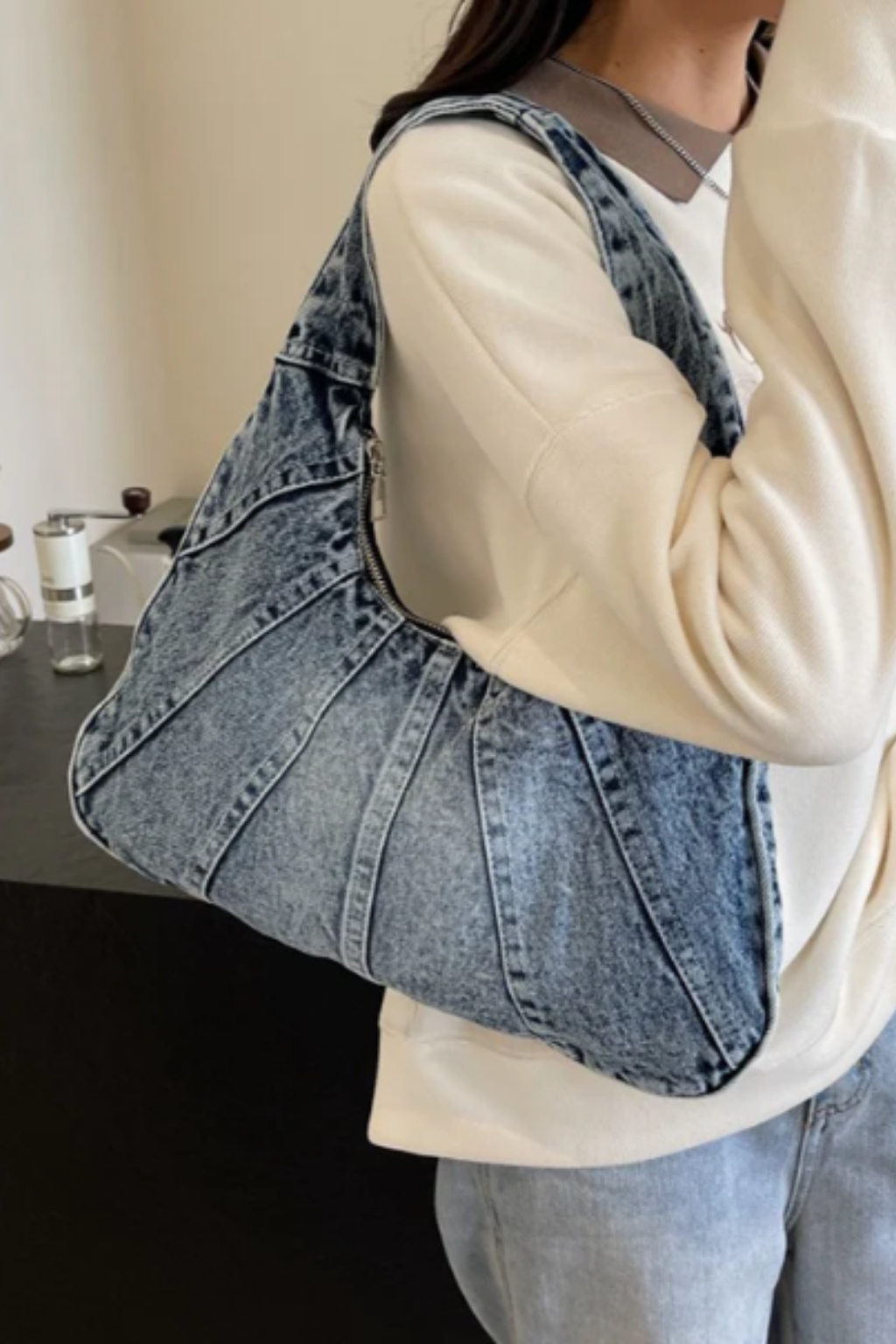 Grand sac hobo en jean bleu, porté à l’épaule avec bandoulière.