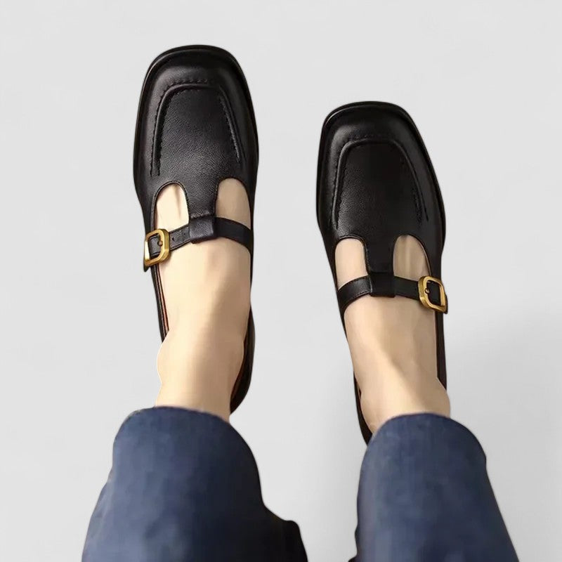 Chaussures bébé à talon bas en cuir noir, bride avant avec boucle dorée.
