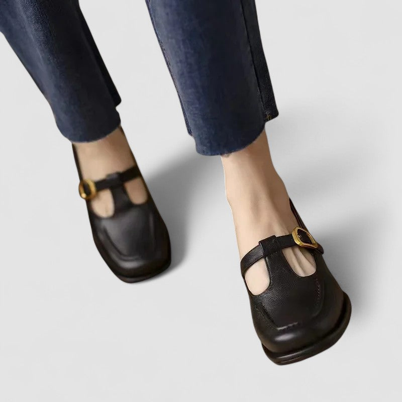 Chaussures bébé à talon bas en cuir noir, bride avant avec boucle dorée.