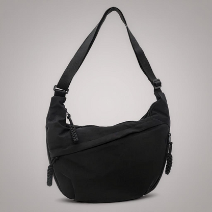 Sac à bandoulière noir en tissu, forme croissant, bandoulière réglable et fermeture zippée.