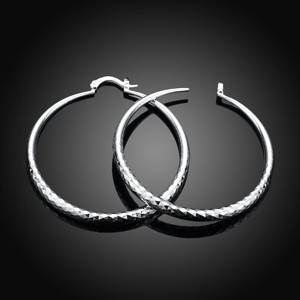 Boucles d’oreilles créoles en argent, face lisse et texture diamantée le long du contour.