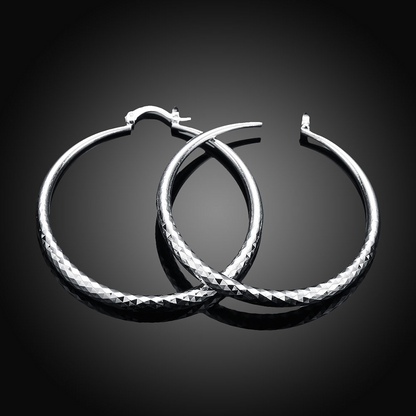 Boucles d’oreilles créoles en argent, face lisse et texture diamantée le long du contour.