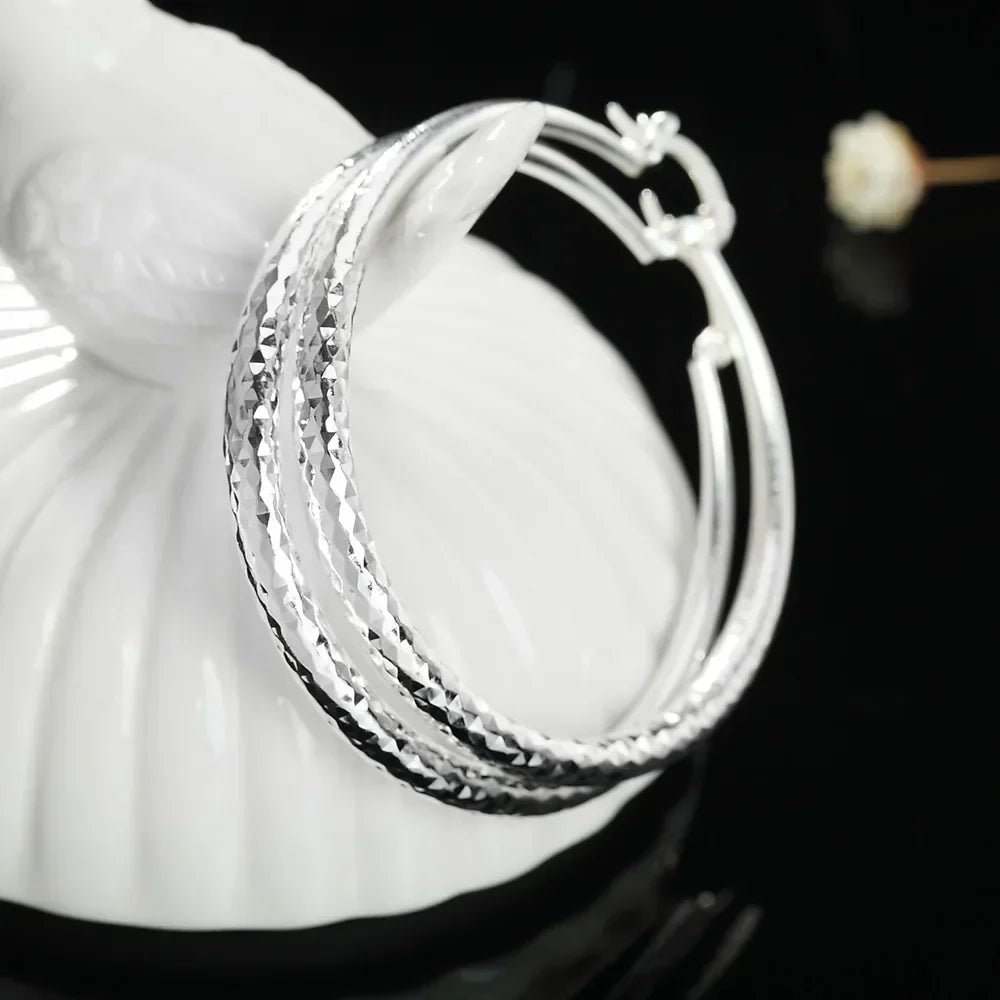 Boucles d’oreilles créoles en argent, gros plan sur la texture losangée de l’anneau.