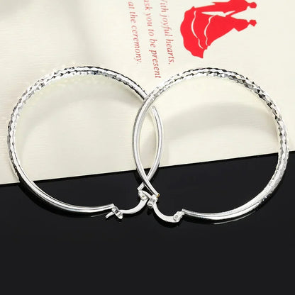 Boucles d’oreilles créoles en argent sterling, relief diamanté sur l’anneau, fermoir visible.