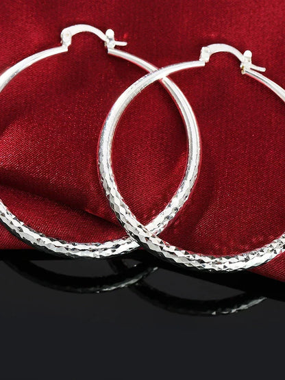 Boucles d’oreilles créoles en argent, motif quadrillé sur l’anneau, attaches visibles.