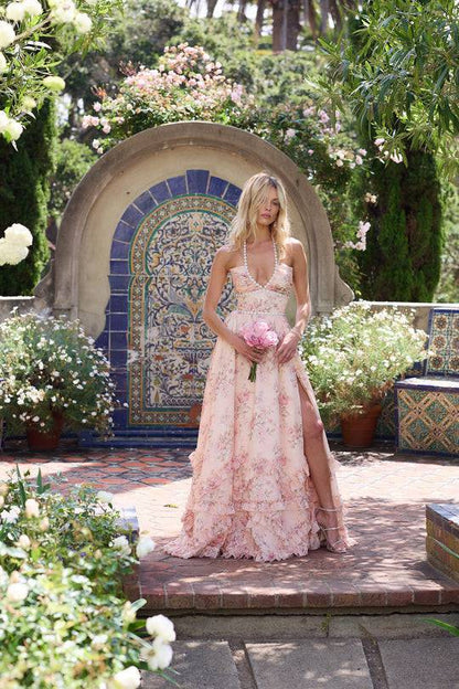 Robe longue rose à motifs floraux, encolure perlée et fente, jupe à volants.