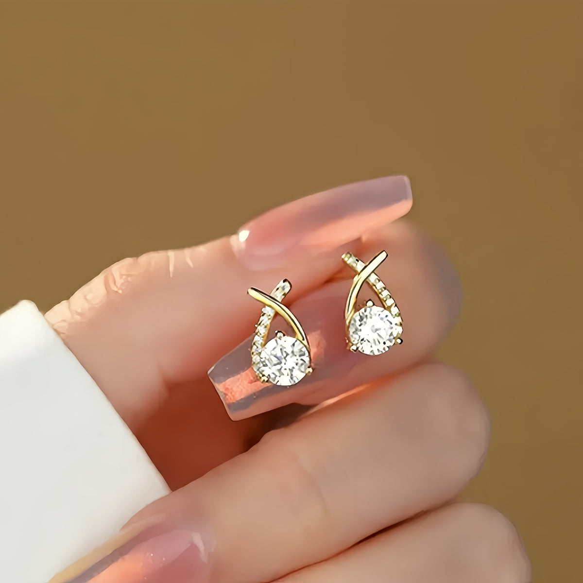 Puces d’oreilles croix dorée en zirconium transparent, présentées sur la main