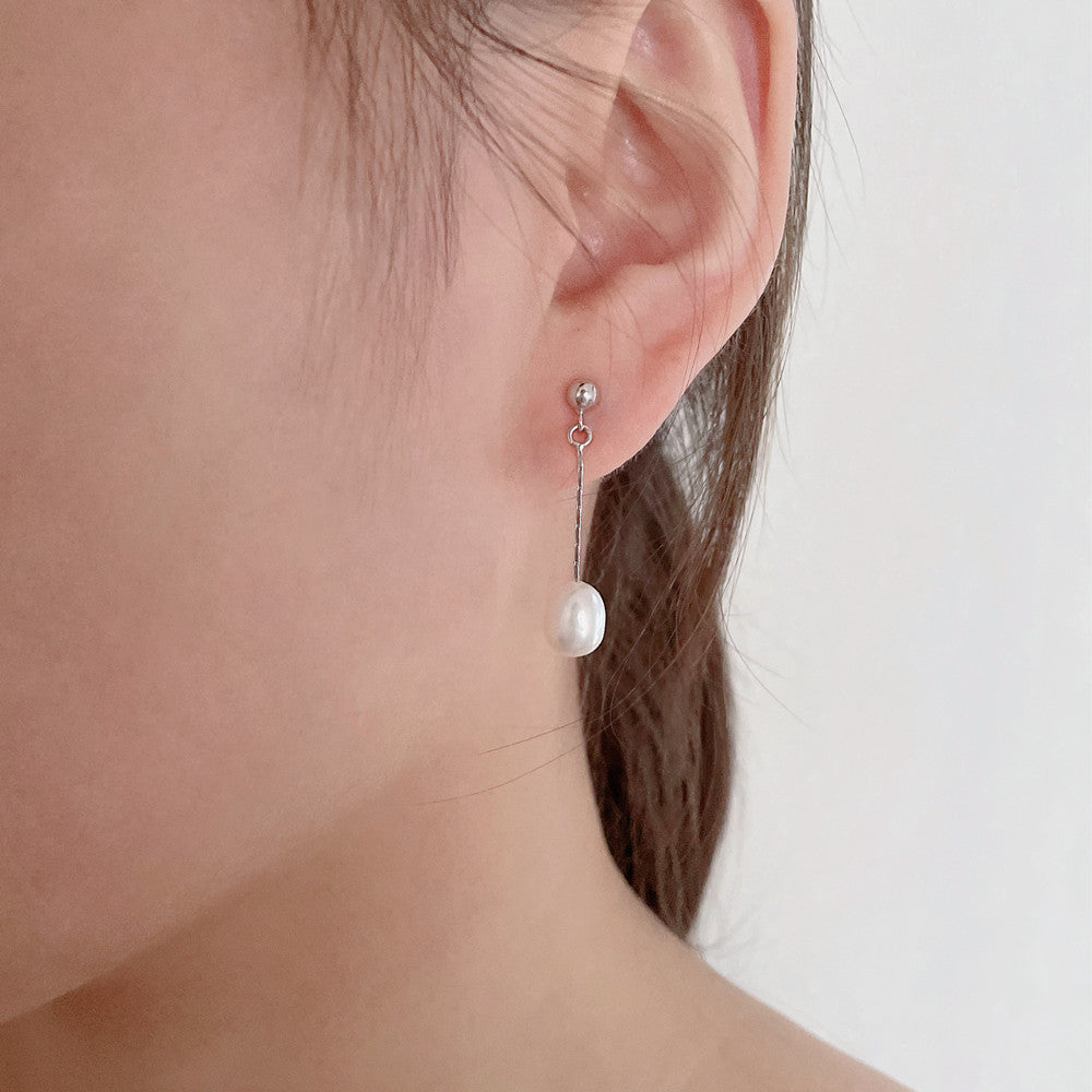 Boucles d’oreilles argentées à perle blanche pendante, aperçu près de l’oreille.