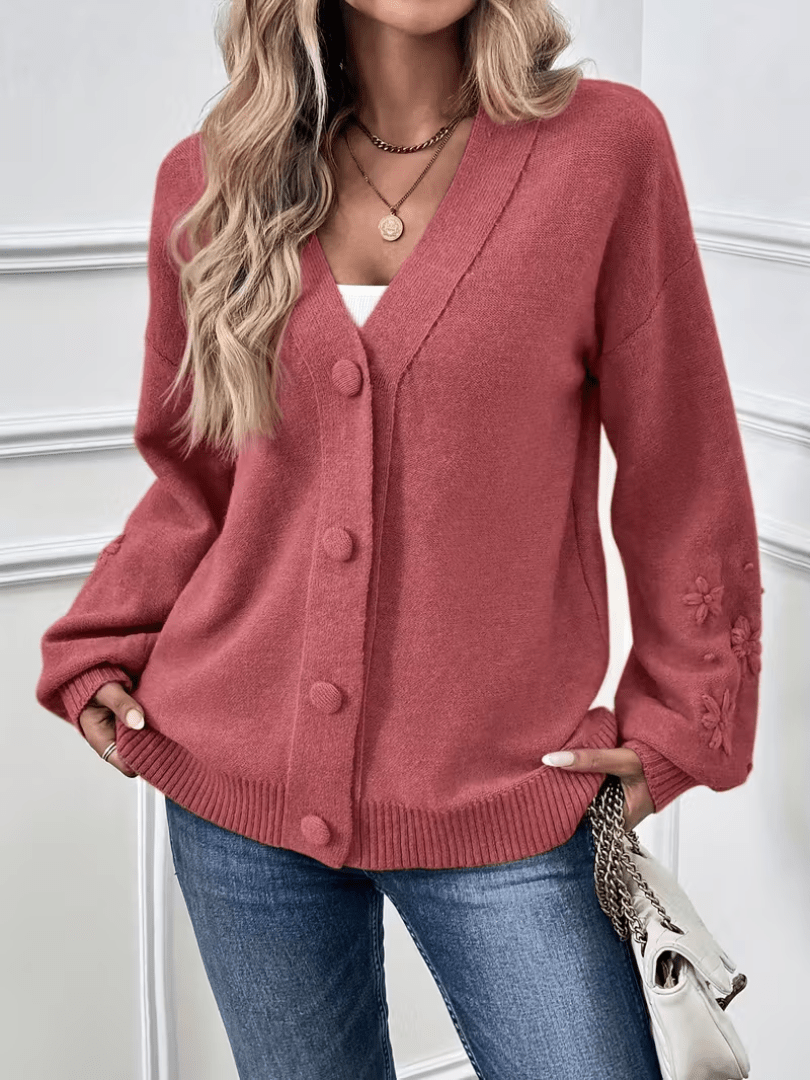 Gilet rose pâle boutonné, col en V, détails floraux sur les manches et poignets.