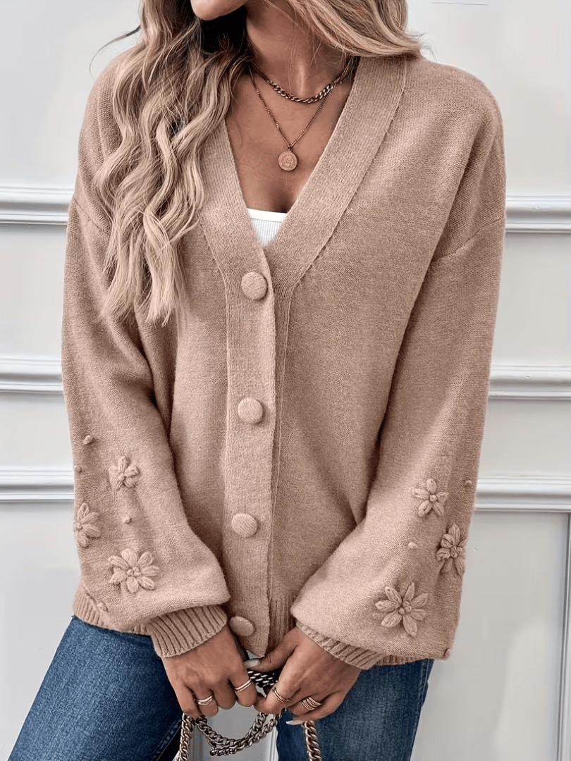 Gilet beige à col V, boutons devant, poignets et manches décorés de fleurs.