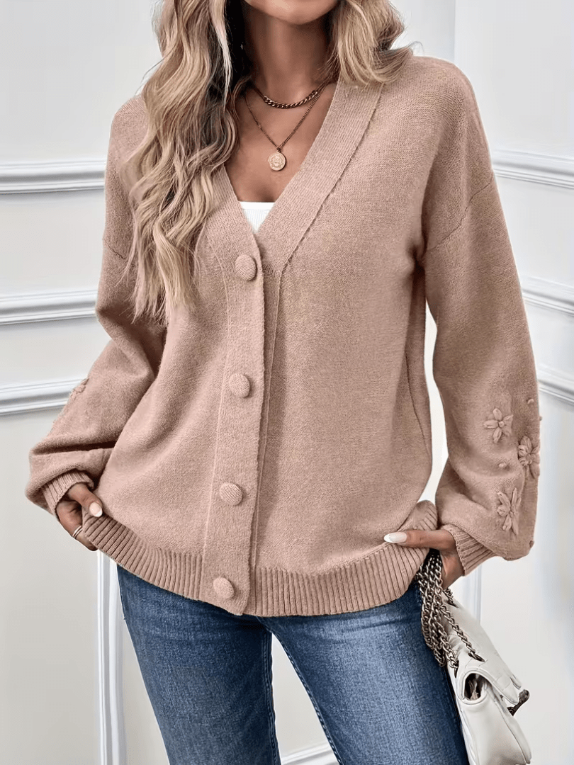 Gilet beige à col V, boutonné, manches et poignets avec décor floral en relief.