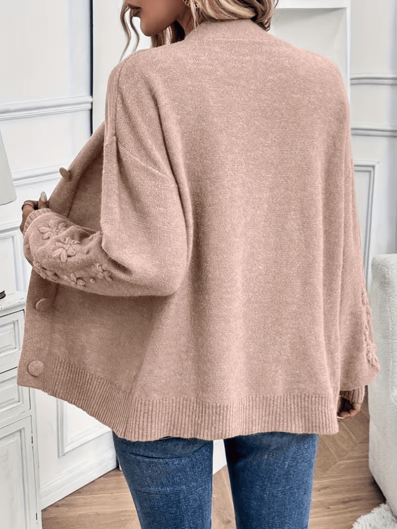 Gilet beige vu de dos, col V, manches bouffantes ornées de fleurs, poignets côtelés.