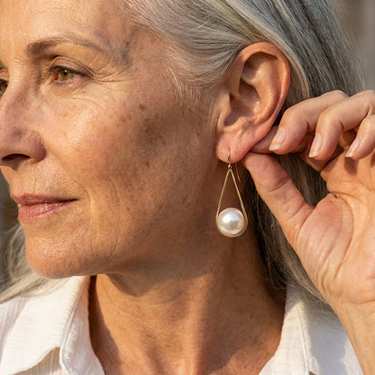 Boucles d’oreilles pendantes perle blanche, monture dorée, portées sur l’oreille