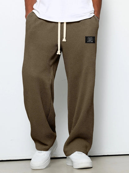 Pantalon pour hommes à coupe confortable marron foncé, taille à cordon, devant fendu, étiquette.