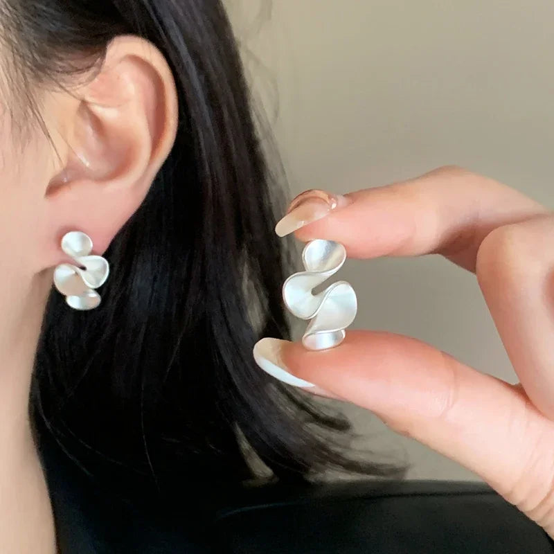 Boucles d’oreilles argentées en forme de trois pétales, portées sur l’oreille