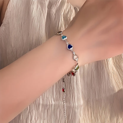 Bracelet doré à cœurs émaillés colorés, porté au poignet près de la main.