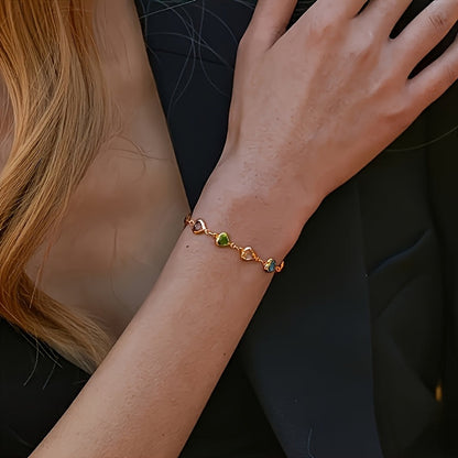 Bracelet doré à breloques cœurs colorés, porté au poignet.