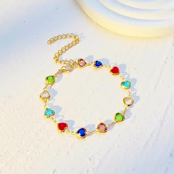 Bracelet doré à cœurs émaillés colorés, posé à plat sur fond clair.