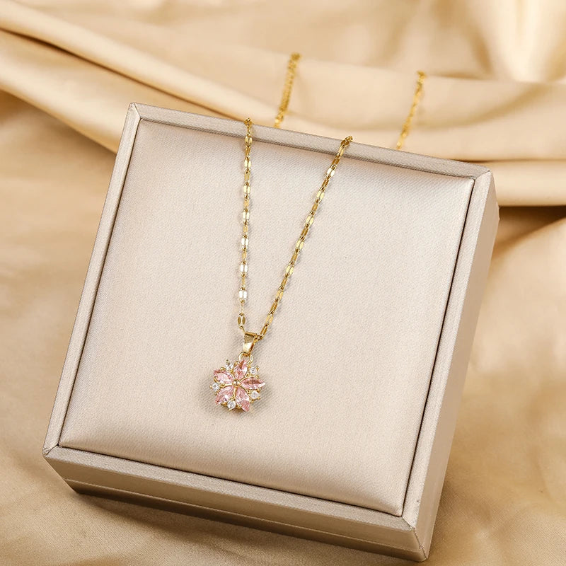Collier doré avec pendentif fleur rose, posé dans une boîte cadeau