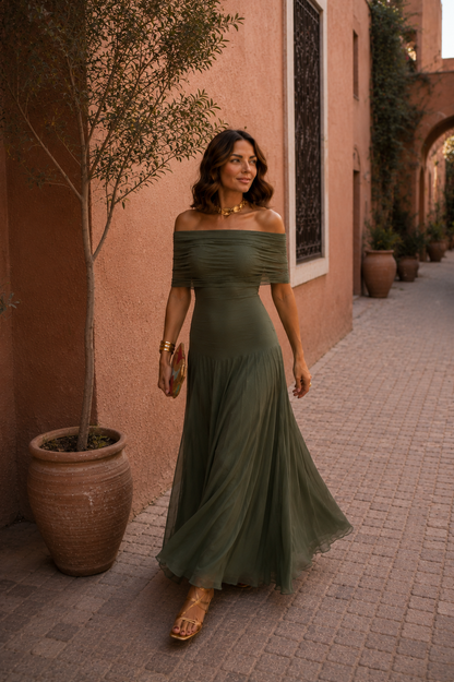 Robe longue vert olive off-shoulder, jupe évasée fluide, buste froncé, sandales visibles.