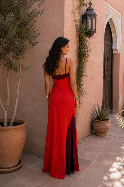 Robe longue rouge, bretelles fines au dos, buste bordeaux et fente latérale.