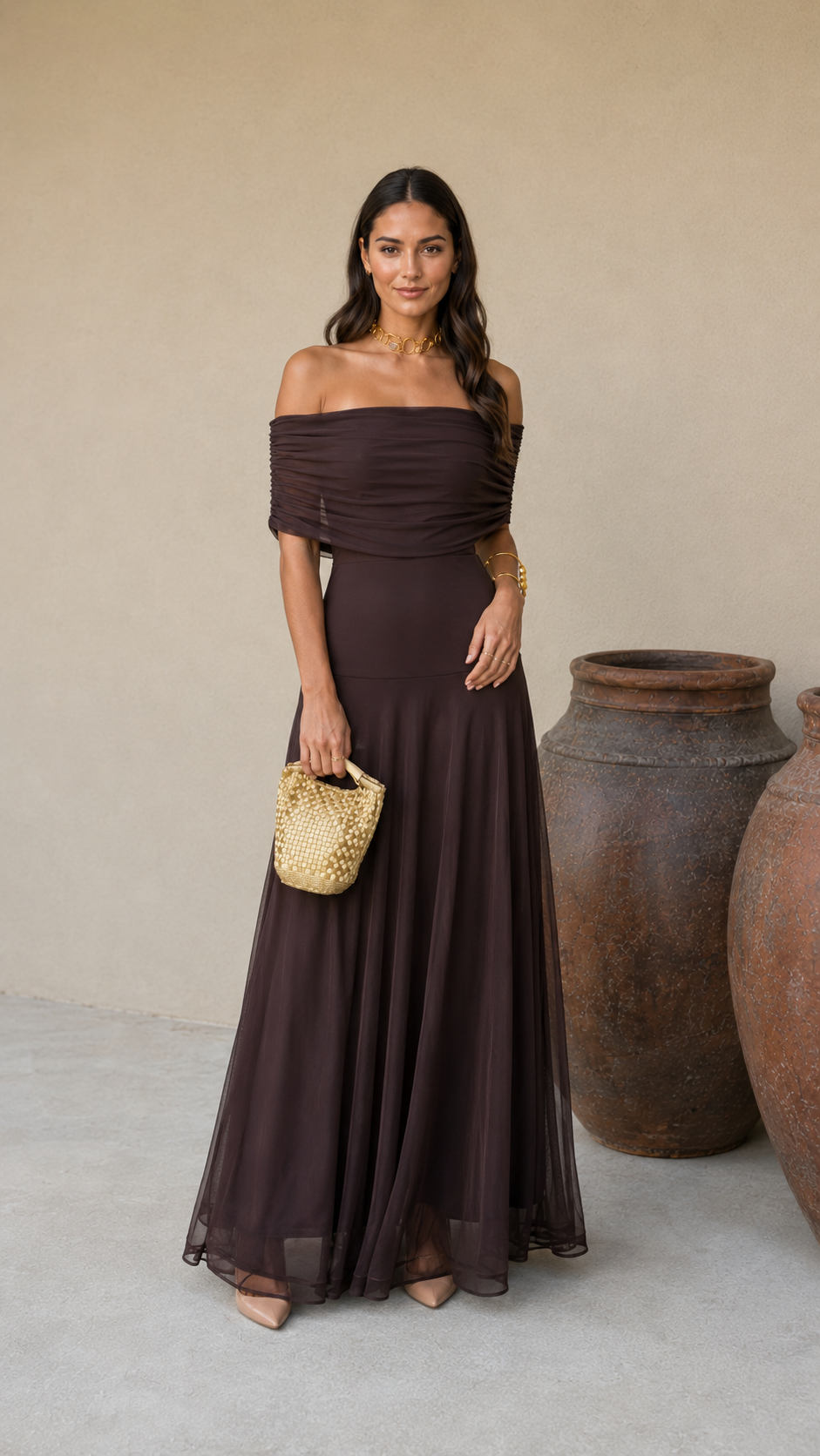 Robe longue marron foncé asymétrique, drapé au buste, pochette dorée en main.