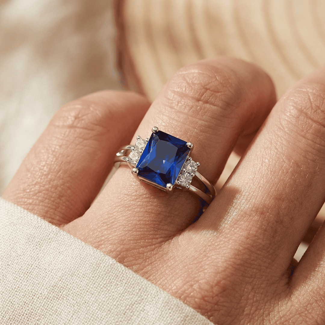 Bague saphir bleu octogonal entouré de pierres sur doigt, monture en or blanc